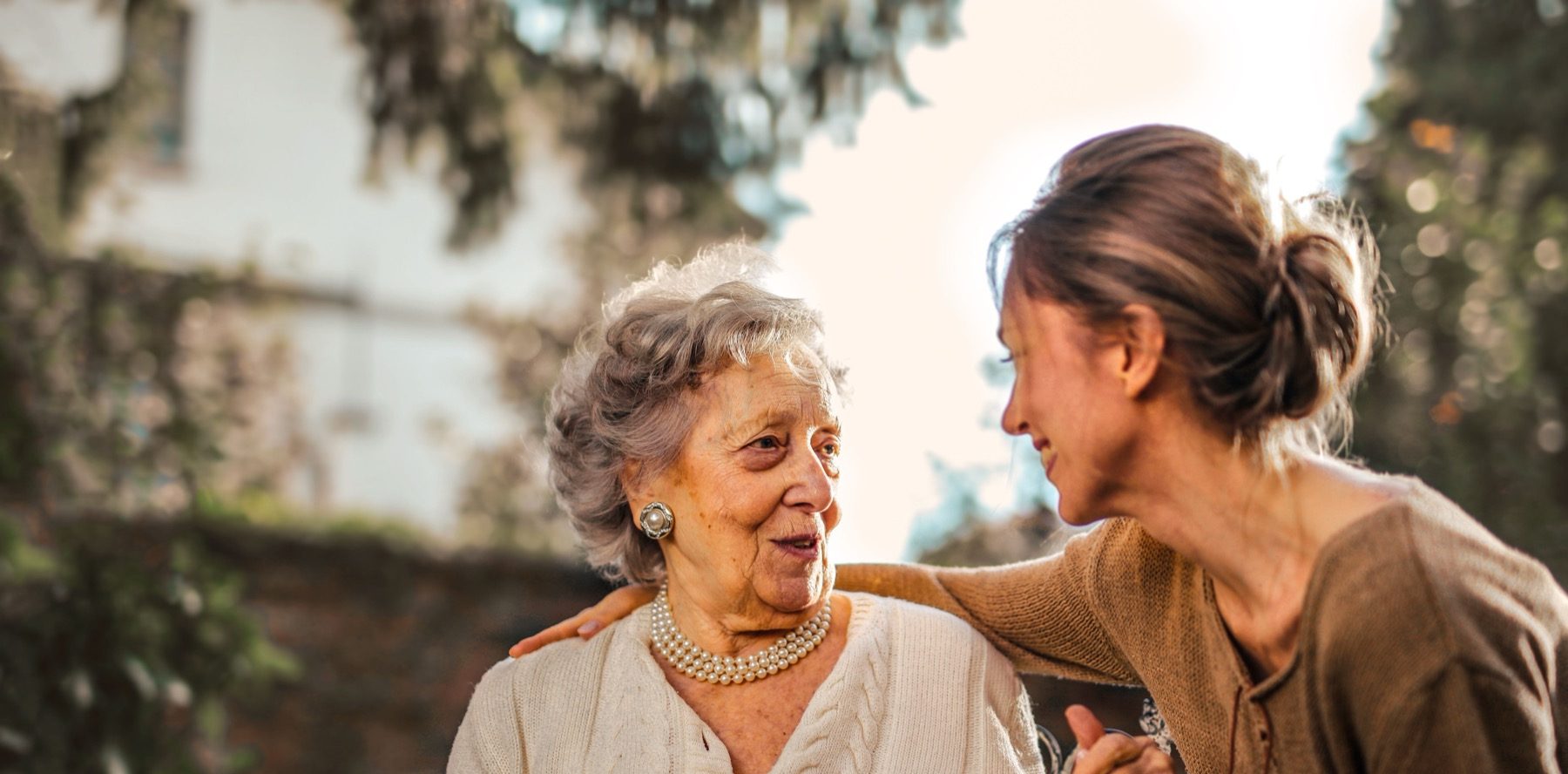 An older woman mid-conversation with a middle-aged woman, sitting together outdoors