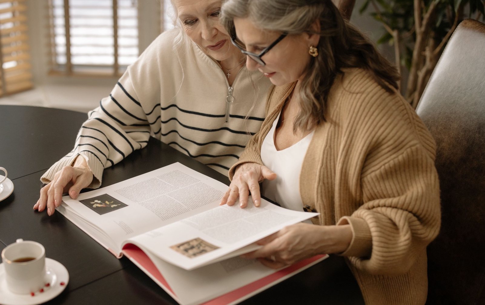 Two women sitting together at a table, looking through pages of written material